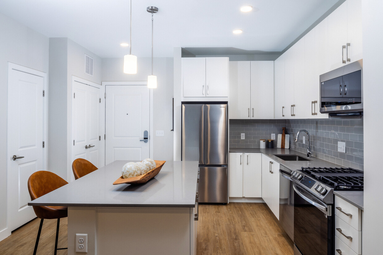 Modern kitchen with white cabinetry, grey tile backsplash, grey quartz countertops, and stainless steel appliances - Avalon North Andover