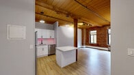Located at 45 Willow St in Springfield, MA, this 2-bedroom, 1-bathroom unit showcases a compelling blend of historic industrial character and modern updates. Soaring wood-planked ceilings with exposed timber beams run throughout the space, complemented by rich exposed brick walls that lend warmth and texture to the open layout. Light-toned hardwood-style flooring ties every room together seamlessly.

The kitchen is well-appointed with white shaker cabinetry, stainless steel appliances including a refrigerator, range, microwave, and dishwasher, plus a central island that doubles as a prep and dining area. A tile backsplash and clean countertops complete the contemporary finish.

The primary bedroom is generously sized, featuring exposed brick, arched windows with natural light, a ceiling fan, and direct access to a secondary room. The second bedroom offers similar architectural detail with wood beam ceilings and ample space. Three closets provide practical storage throughout the unit.

The bathroom is finished with hexagonal tile flooring, marble-look wall surrounds, a soaking tub with shower, and matte black fixtures paired with a green vanity for a modern aesthetic. The hallway entrance connects all areas efficiently, rounding out this distinctive, character-rich home.
