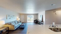 This single-floor residence offers a thoughtfully designed open-concept layout that connects the main living spaces seamlessly. The living room is bright and welcoming, featuring dark hardwood-style flooring, neutral-toned walls, and a sliding glass door that opens to a private patio, allowing natural light to flow throughout the space. A dedicated dining area adjacent to the living room includes a ceiling fan and wood-style flooring, creating a comfortable setting for meals.

The kitchen is well-equipped with white shaker-style cabinetry, light quartz countertops, stainless steel appliances including a range, microwave, and refrigerator, and a functional peninsula that overlooks the living area. The layout provides ample counter and storage space for everyday use.

The bedroom is carpeted and comfortably sized, featuring a ceiling fan and a window with an exterior view, providing natural light. A flexible secondary room with carpet, a ceiling fan, and a window serves well as a home office or additional bedroom.

Two bathrooms are finished with wood-style flooring, white cabinetry, and light countertops. The primary bathroom includes a walk-in shower, while the second bathroom features a tub-shower combination. Both offer practical storage solutions with wall-mounted cabinetry.