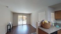 This single-floor residence offers a thoughtfully designed layout that balances open living with functional private spaces. The living room is a welcoming focal point, featuring rich dark hardwood-style flooring, neutral gray walls, and a sliding glass door fitted with vertical blinds that floods the room with natural light and provides access to an outdoor patio area. The open flow between the living room and kitchen creates a cohesive common area ideal for everyday living. The kitchen is well-equipped with warm medium-toned wood cabinetry, granite-style countertops, and black appliances including a range, dishwasher, and refrigerator. A peninsula counter adds additional prep space and serves as a natural transition between the kitchen and living areas. The bedroom is a calm, neutral retreat with plush wall-to-wall carpeting and a window with blinds that allows for comfortable natural light. The bathroom features hardwood-style flooring, a full-size bathtub with a shower curtain enclosure, a toilet, and towel bars, all finished in clean, neutral tones. Throughout the residence, consistent neutral wall colors and clean white trim create a cohesive and move-in-ready aesthetic.