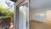 This single-floor residence is set within a thoughtfully landscaped community that immediately impresses with its natural surroundings. Tall, mature trees tower above the property, providing generous shade and a sense of established character throughout the grounds. Winding concrete pathways meander through well-tended garden beds filled with a diverse mix of shrubs, ground cover, and flowering plants, creating a serene, park-like atmosphere from the moment of arrival.

The exterior of the building features a neutral stucco finish complemented by wood-accented balconies and trim, reflecting a classic mid-century influenced architectural style. The unit's entry is particularly inviting, with a distinctive teal front door adorned with a decorative wreath, framed by lush, overhanging foliage that adds privacy and charm. The interplay of the natural landscaping with the built environment gives the property a secluded, tranquil feel despite being part of a larger complex.

The surrounding communal outdoor spaces are well-maintained, with layered plantings that provide year-round greenery and visual interest. The mature tree canopy filtering natural light across the pathways and garden areas enhances the overall ambiance, making the approach to the home a pleasant and scenic experience. This property offers a harmonious blend of comfortable residential living and lush natural beauty.