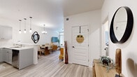 This well-designed single-floor residence offers a cohesive open-concept layout that seamlessly connects the living, dining, and kitchen areas. Light wood-look flooring flows throughout the main living spaces, complementing the crisp white walls and creating a clean, airy aesthetic.

The kitchen is outfitted with gray shaker-style cabinetry, a white countertop peninsula with bar seating, and a full suite of stainless steel appliances, including a French door refrigerator, electric range, and over-the-range microwave. Pendant lighting above the peninsula adds a modern touch, while a set of double panel doors provides additional storage.

Adjacent to the kitchen, the dining area accommodates a full-sized table and is lit by a contemporary chandelier. A decorative mirror accents the wall, tying the space together. The living room features large sliding glass doors that invite abundant natural light and open the space visually. A sectional sofa, media console, and open shelving unit furnish the room comfortably.

The bedroom offers plush carpeting and ample wall space, with warm wood furnishings contributing to a relaxed, grounded atmosphere. The bathroom is finished with gray vanity cabinetry, a white countertop, a framed mirror, and wood-look tile flooring, completing this thoughtfully appointed residence.