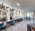 This contemporary office space, located at 3351 Walton Road in Corinth, Texas, offers a compact yet efficiently designed 470 square feet of professional environment. The space is characterized by its modern aesthetic, featuring a harmonious blend of functionality and style.

Upon entry, visitors are greeted by a sleek reception area with a striking black desk, set against a backdrop of abstract artwork and textured walls. The grey patterned carpet adds visual interest and flow throughout the space.

Adjacent to the reception is a well-appointed conference room, enclosed by glass walls for transparency and natural light. The room is furnished with a wooden table and comfortable blue chairs, ideal for meetings and presentations. A statement lighting fixture, reminiscent of interlocking golden rings, serves as both illumination and art.

The open workspace area showcases a unique design element: a feature wall with geometric white lines contrasting against a wood-toned background. This area is equipped with individual workstations, each outfitted with modern blue ergonomic chairs and ample desk space. Pendant lights with wooden accents hang above, providing focused illumination.

Throughout the office, recessed lighting and large windows ensure a bright, welcoming atmosphere. The color palette of whites, blues, and wood tones creates a cohesive and professional ambiance. This thoughtfully designed space maximizes its 470 square feet, offering a balance of private and collaborative areas suitable for a variety of business needs.