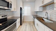 Located at 1231 S Bundy Dr in the desirable West Los Angeles neighborhood of 90025, this single-floor unit showcases a clean, modern aesthetic with thoughtfully updated finishes throughout. Light wood-tone luxury vinyl plank flooring runs continuously across the living areas, bedroom, and hallways, lending a cohesive and contemporary feel to the entire space.

The living area is bright and open, with large sliding glass doors fitted with vertical blinds that allow abundant natural light to pour in. A wall-mounted air conditioning unit provides climate control comfort. The layout flows naturally into the adjoining spaces, offering a functional and well-connected floor plan.

The galley-style kitchen is a standout feature, outfitted with crisp white shaker cabinetry, dark quartz countertops, and a geometric patterned tile backsplash. Stainless steel appliances, including a refrigerator, range, and dishwasher, complete the space, while a window above the sink brings in natural light.

The bedroom is generously proportioned, featuring a wide window with blinds, an open closet with built-in shelving, and its own wall-mounted air conditioning unit. Additional rooms provide flexible use as a second bedroom or office, each with clean white walls and ample natural light.

The bathroom features full subway tile surrounds in the tub/shower combination, a window for ventilation, and tile flooring, rounding out this well-appointed unit.