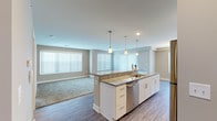 This single-floor residence offers a thoughtfully designed open-concept layout that seamlessly connects the kitchen and living areas. The kitchen is a functional centerpiece, featuring a large island with granite countertops, an undermount sink, and pendant lighting overhead. White shaker-style cabinetry provides generous storage, while stainless steel appliances — including a gas range, microwave, refrigerator, and dishwasher — complete the space. Light wood-look vinyl plank flooring runs throughout the kitchen and living areas, creating a cohesive aesthetic.

The open living area extends from the kitchen, bathed in natural light from multiple large windows dressed with vertical blinds. Plush carpeting in the living and bedroom spaces adds warmth and comfort. The bedrooms are well-sized, each featuring carpet flooring, neutral-toned walls, and windows that invite natural light.

The bathroom is finished with large-format grey tile surrounding a soaking tub and shower combination, complemented by a built-in niche for storage. A practical in-unit stacked washer and dryer is conveniently located in the hallway. The overall palette of soft greys and warm neutrals gives the space a clean, modern, and welcoming ambiance throughout.