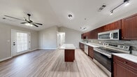 Located at 3301 London Ct in Aiken, South Carolina, this single-story, 2-bedroom, 2-bathroom home offers a thoughtfully designed layout with modern finishes throughout. Light-toned wood-look flooring flows seamlessly across the entire living space, creating a cohesive and clean aesthetic.

The open-concept kitchen is a standout feature, showcasing rich dark wood cabinetry, stone tile backsplash, granite-look countertops, and a full suite of stainless steel appliances including a refrigerator, range, microwave, and dishwasher. A freestanding kitchen island provides additional prep and serving space. Vaulted ceilings in the kitchen and living area lend an airy, spacious feel, complemented by track lighting and a ceiling fan.

The bedrooms are comfortably sized, each receiving natural light from large windows with views of surrounding greenery. The generously proportioned primary bedroom includes a walk-in closet with dual wire shelving systems for ample storage. Both bathrooms feature tub-shower combinations with matte black fixtures and wood-look tile flooring.

A dedicated laundry room accommodates a full-size washer and dryer with overhead shelving. The hallway connects all rooms efficiently, making the layout practical and easy to navigate.