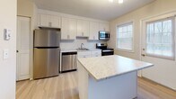 This three-floor property is thoughtfully designed with updated finishes and functional spaces across every level. The basement level provides substantial utility, featuring a large open area with a garage door, painted concrete floors, built-in shelving, and dedicated mechanical space housing the electrical panel, sump pump, and ventilation systems. A separate unfinished room offers additional storage or flexible use potential.

The main living level showcases a renovated kitchen equipped with white shaker cabinetry, marble-style quartz countertops, stainless steel appliances including a refrigerator, dishwasher, range, and microwave, and a central island for additional workspace. Light wood-tone flooring runs throughout the main level, complementing the neutral wall tones. A half bathroom with a pedestal sink and wood-look flooring adds convenience on this floor.

The upper level hosts multiple bedrooms, each featuring either warm hardwood or light laminate flooring and windows that provide natural light and outdoor views. One bedroom includes dual closets. The upper-level bathroom is finished with subway tile in the walk-in shower, wood-look flooring, and brushed nickel fixtures, delivering a clean, modern aesthetic throughout.
