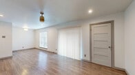 This single-story space is designed with a clean, neutral aesthetic that creates a bright and functional living environment. Wood-look flooring runs consistently throughout the main living areas and bedrooms, lending warmth and visual continuity to the interior.

The main living area is open and well-lit, featuring recessed lighting, a ceiling fan, and multiple windows dressed with horizontal blinds. A large sliding glass door with vertical blinds allows additional natural light and provides exterior access. An electrical panel is conveniently integrated into one wall of the living space.

The kitchen is efficiently laid out with white cabinetry, dark granite countertops, a decorative tile backsplash, and a full suite of stainless steel appliances including a refrigerator, range, microwave, and dishwasher. A window above the counter brings in natural light.

The bedroom is a comfortable, well-proportioned room with its own ceiling fan, a window with blinds, and the same wood-look flooring found throughout the unit.

The bathroom features white cabinetry with dark granite countertops, a vessel-style sink, and a separate water closet with a soaking tub framed by marble-look tile surround, offering a clean and polished finish overall.