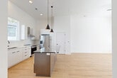 Located at 411 Charles Ave in Charlotte's vibrant Plaza Midwood neighborhood, this contemporary 3-story home offers a thoughtfully designed layout spread across three floors. The ground level houses a spacious attached garage with a utility room, providing convenient access to the home's interior. The main living level features an open-concept kitchen and dining area highlighted by light hardwood floors, soaring ceilings, and an abundance of natural light. The kitchen is appointed with white cabinetry, a subway tile backsplash, stainless steel appliances including a gas range and refrigerator, a wall-mounted range hood, and a striking center island with a dramatic dark stone countertop accented by elegant veining. Pendant lighting adds a modern touch overhead. The upper floors accommodate two well-proportioned bedrooms, each featuring hardwood flooring, natural light from large windows, and ceiling fans. The primary bedroom includes its own dedicated closet. Four bathrooms are distributed throughout the home, with standout bathrooms showcasing geometric patterned tile flooring, dark stone vanity tops, gold and matte black fixtures, glass-enclosed walk-in showers, and white subway tile walls. Clean white walls and natural wood staircases with modern horizontal railings unify the home's contemporary aesthetic throughout all three levels.