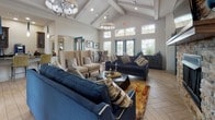 This expansive single-floor clubhouse is thoughtfully designed to serve as a dynamic community gathering space, offering a diverse range of amenities across several distinct areas. The main lounge is an inviting, open-plan space anchored by a dramatic floor-to-ceiling stacked stone fireplace with a mounted flat-screen TV and a wood mantle. Soaring vaulted ceilings with exposed white-painted beams, elegant chandelier lighting, and an abundance of natural light from large windows and glass doors create an airy, welcoming atmosphere. Comfortable navy blue sofas and neutral wingback chairs are arranged throughout, all resting on light wood-look tile flooring that flows seamlessly through the entire facility.

The game room is a standout feature, housing both a classic billiards table beneath a modern orb pendant light and a full-size ping-pong table in a dedicated space with a coffered dark ceiling. A cozy lounge nook offers two leather egg chairs and a wall-mounted TV. The fully equipped kitchen includes dark granite countertops, rich wood cabinetry, and stainless steel appliances, with pass-through windows overlooking an outdoor area. A dedicated business center provides multiple computer workstations along a granite-topped desk, offering a productive workspace within the facility.