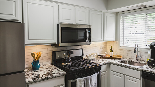 Un moderno placa para salpicaduras de azulejos blancos y gabinetes de color blanco de búsqueda de coincidencias adornan nuestros apartamentos renovados - Alister Falls Church