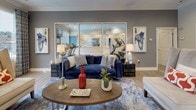 This single-level lobby is thoughtfully designed to serve as both a welcoming gathering space and a functional community hub. Light hardwood flooring extends throughout, complemented by warm gray and neutral wall tones that create a cohesive, modern aesthetic. Crown molding and recessed lighting add refined architectural detail to the space.

The lounge area anchors the lobby with a rich navy velvet sofa, accent chairs, and a circular wooden coffee table styled with decorative accessories. Large windows dressed with patterned drapery flood the area with natural light while offering views of the outdoor pool and surrounding landscape. Framed abstract artwork adorns the walls, reinforcing the contemporary design scheme.

Adjacent to the lounge, a glass-partitioned wall reveals a fitness center equipped with cardio machines, allowing visual connectivity while maintaining separation. A dedicated dining nook features a rustic wood table with upholstered chairs, surrounded by windows that bring in additional natural light.

The leasing office area is accessible through both glass-front sliding doors and a private entry, providing a professional yet approachable environment. A decorative console and round mirror near the entrance contribute to the polished, welcoming character of this lobby.
