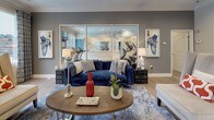 This single-level lobby is thoughtfully designed to serve as both a welcoming gathering space and a functional community hub. Light hardwood flooring extends throughout, complemented by warm gray and neutral wall tones that create a cohesive, modern aesthetic. Crown molding and recessed lighting add refined architectural detail to the space.

The lounge area anchors the lobby with a rich navy velvet sofa, accent chairs, and a circular wooden coffee table styled with decorative accessories. Large windows dressed with patterned drapery flood the area with natural light while offering views of the outdoor pool and surrounding landscape. Framed abstract artwork adorns the walls, reinforcing the contemporary design scheme.

Adjacent to the lounge, a glass-partitioned wall reveals a fitness center equipped with cardio machines, allowing visual connectivity while maintaining separation. A dedicated dining nook features a rustic wood table with upholstered chairs, surrounded by windows that bring in additional natural light.

The leasing office area is accessible through both glass-front sliding doors and a private entry, providing a professional yet approachable environment. A decorative console and round mirror near the entrance contribute to the polished, welcoming character of this lobby.
