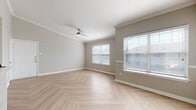 This single-floor residence showcases a thoughtfully designed layout with a consistent neutral color palette that creates a bright, cohesive atmosphere throughout. The main living area is a standout feature, boasting light-toned herringbone-patterned flooring that adds visual depth and elegance. Crown molding frames the ceiling, while multiple windows dressed with horizontal blinds invite generous natural light. A ceiling fan enhances comfort and airflow in the living space.

The kitchen is equipped with white cabinetry featuring matte black hardware, quartz-look countertops with subtle veining, and stainless steel appliances including a refrigerator and dishwasher. A pass-through countertop connects the kitchen to the adjacent living area, enhancing the open feel.

The bedrooms are carpeted in a plush, neutral tone and each features a ceiling fan and window for natural light. The rooms offer ample space and a calm, restful ambiance. The bathroom is finished with floor-to-ceiling wood-grain tile surrounding a soaking tub and shower combination, complemented by herringbone flooring that mirrors the main living area. White cabinetry provides practical storage. Overall, the space presents a clean, modern aesthetic with quality finishes throughout.