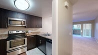 This single-floor residence offers a practical and modern layout with thoughtfully designed spaces throughout. The kitchen is a functional highlight, featuring dark espresso cabinetry with sleek bar-pull hardware, granite-style countertops, and a full suite of stainless steel appliances including an electric range, over-the-range microwave, dishwasher, and refrigerator. A peninsula counter with a double sink provides additional workspace and opens toward the living area, enhancing the sense of connectivity between spaces. The living area is generously sized, finished with warm hardwood-style flooring and neutral-toned walls that create a bright, inviting ambiance. A separate carpeted room offers flexibility as a bedroom or secondary living space, with natural light visible from an exterior-facing window or sliding door. The bathroom is well-equipped with a full tub and shower combination, granite-style countertops, a single vanity sink, and wood-look flooring. A standout feature is the walk-in closet, which provides ample storage with multi-tiered shelving rods along three walls and durable hardwood-style flooring. The overall design is cohesive, with consistent finishes and a neutral color palette throughout.