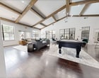 Located at 1020 Scotland Dr in DeSoto, TX, this 1,550 square foot single-floor office space combines sophisticated design with practical functionality. The space is defined by soaring vaulted ceilings adorned with rich, dark exposed wood beams that carry throughout, creating a dramatic yet welcoming architectural statement. Dark hardwood floors run continuously across the entire floor plan, anchoring the warm, modern-rustic aesthetic.

The main lounge area serves as a central gathering space, featuring a striking floor-to-ceiling natural stone fireplace, large plantation-shuttered windows that regulate natural light, and ample seating. A full-size billiards table adds a recreational element to the open common area, which is bathed in light from oversized steel-framed windows.

The dedicated office area includes a private workstation with shuttered windows, a bold accent wall in deep slate gray, and direct sightlines into the main lounge through interior steel-frame glass partitions. The fully equipped kitchen features rich dark wood cabinetry, granite countertops, stainless steel appliances including a full-size refrigerator, a wine cooler, and a bar-height counter with leather bar seating — ideal for hosting and day-to-day convenience.