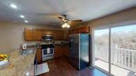 This three-floor home offers a thoughtfully designed layout with a variety of functional and comfortable living spaces spread across its multiple levels. The kitchen is a standout feature, equipped with stainless steel appliances including a refrigerator, range, and over-the-range microwave, all complemented by warm wood cabinetry and granite countertops. Rich hardwood flooring runs throughout the kitchen, which also benefits from direct access to a balcony overlooking a scenic, wooded landscape — an ideal setting for enjoying natural surroundings. A ceiling fan with integrated lighting adds both comfort and practicality to the space. The living areas are generously sized, featuring plush carpeting, ceiling fans, recessed lighting, and sliding glass door access to the outdoors, allowing abundant natural light to fill the rooms. A staircase with a white balustrade connects the floors, as seen in the open layout overview. Bedrooms are carpeted and include closets with built-in rod storage. The bathrooms are well-equipped, with one featuring a double-sink vanity with a marble-style countertop and a shower-tub combo, another offering a single-sink vanity with tile flooring, and a half bath with hardwood flooring. Neutral warm tones carry throughout, creating a cohesive and inviting atmosphere across the entire home.