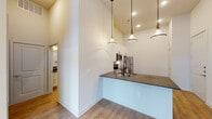 This single-story space is defined by its impressively tall vaulted ceilings, which lend an airy, open quality throughout the main living areas. The kitchen serves as a central highlight, featuring white shaker-style cabinetry, dark granite countertops, and a classic white subway tile backsplash. Stainless steel appliances—including a refrigerator, electric range, over-the-range microwave, and dishwasher—provide a modern, functional aesthetic. A peninsula with an integrated sink and matte black fixtures extends into the living area, creating a natural gathering point. A trio of pendant lights with barn-style shades hangs above, adding warmth and character.

The open living area flows seamlessly from the kitchen and is anchored by light wood-look flooring, a ceiling fan, and a set of French doors that allow natural light to pour in. The bedroom offers a quieter retreat with plush carpet flooring and a large window. The bathroom is finished with white cabinetry, dark granite countertops, wood-look flooring, and subway tile in the shower area. A dedicated laundry area accommodates full-size Whirlpool washer and dryer units, adding everyday convenience. Throughout, the neutral color palette and clean finishes create a cohesive, modern atmosphere.