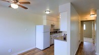 This single-floor space offers a clean, functional layout with an open-concept design that connects the kitchen and living area seamlessly. The kitchen is outfitted with white cabinetry, a dark countertop, a sink, and full-sized appliances including a refrigerator. A partial wall with a breakfast bar counter serves as a natural divider between the kitchen and the adjoining living space, adding both definition and convenience to the layout. The flooring throughout features warm hardwood-style planks that contribute to a cohesive and inviting atmosphere. Neutral-toned walls keep the interior feeling bright and airy, while flush-mount ceiling lighting ensures consistent illumination. A ceiling fan is visible in the living area, providing both comfort and airflow. The space benefits from a straightforward, efficient design that prioritizes practicality while maintaining a comfortable and welcoming ambiance. Overall, the layout makes good use of its footprint, offering an approachable and livable environment with thoughtful details throughout.