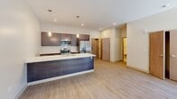 This 600-square-foot, one-bedroom, one-bathroom apartment in Pittsburgh, PA (15201) delivers a modern, open-concept layout with clean lines and contemporary finishes throughout. The main living area features light-toned hardwood flooring, recessed lighting, exposed ductwork accents, and large windows with a glass-panel entry door that flood the space with natural light and offer views of the surrounding neighborhood. The open kitchen is a standout feature, boasting a large island with a white quartz countertop and undermount sink, dark espresso cabinetry, stainless steel appliances including a refrigerator, range, and microwave, and stylish pendant lighting overhead. The kitchen flows seamlessly into the living area, making the space ideal for entertaining. The 170-square-foot bedroom is carpeted for comfort and includes a large window with an outdoor view, a walk-in closet with a hanging rod, and direct access to the rest of the unit. The bathroom is finished with clean white tile, a full soaking tub and shower combination, a dark-cabinetry vanity with a white countertop, and a framed mirror. The unit's neutral color palette and modern fixtures create a bright, functional, and inviting atmosphere throughout.