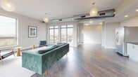 Located at 2525 E Main St in Richmond, Virginia, this contemporary single-floor space offers a well-designed open-plan layout ideal for gathering, working, or entertaining. The interior is defined by large-format tile flooring throughout, crisp white walls, and exposed industrial-style ductwork that adds a modern, loft-inspired character to the space.

The kitchenette area is outfitted with sleek white cabinetry, dark granite countertops, a stainless steel sink, full-size refrigerator, dishwasher, and microwave — providing all the essentials for hosting and catering needs. Bar-height seating along the counter offers a casual dining option.

A dedicated lounge area features comfortable seating, including a striking green velvet sofa, anchored beneath globe pendant lighting. This area opens toward expansive windows and glass doors that lead to an outdoor balcony, flooding the space with natural light and offering sweeping views of the surrounding Richmond cityscape.

Adjacent to the lounge, a dining or meeting area accommodates a full-sized table with upholstered chairs, framed by large windows on two sides that capture wide, elevated views of the city and beyond. Recessed lighting, globe pendant fixtures, and curated artwork complete the polished yet approachable aesthetic of this versatile space.