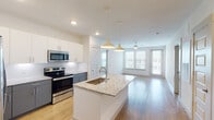 This single-floor residence showcases a thoughtfully designed open-concept layout that seamlessly connects the kitchen and living areas. The kitchen serves as the heart of the space, anchored by a large central island topped with granite countertops and fitted with an undermount sink. Pendant lights hang above the island, providing focused illumination. The kitchen is equipped with stainless steel appliances, including a range, microwave, and refrigerator, complemented by two-toned cabinetry featuring white upper cabinets and gray lower cabinets, along with a classic tile backsplash.

The open living area extends naturally from the kitchen, bathed in natural light through multiple windows fitted with horizontal blinds. A ceiling fan maintains airflow throughout the shared space. Hardwood-style flooring runs through the main living and kitchen areas, lending warmth and continuity.

The bedrooms are carpeted for comfort and each features a ceiling fan and windows that bring in natural light. The primary suite connects directly to a hallway that leads to a bathroom with granite-topped dual vanity cabinetry and a walk-in closet with built-in shelving. The overall aesthetic is clean, contemporary, and neutral throughout.