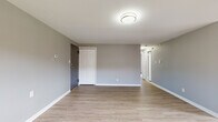 This single-floor unit offers a clean, contemporary design highlighted by light hardwood-style flooring throughout the main living areas and a neutral gray color palette that lends a cohesive, modern feel. The open layout connects the living area to the kitchen, creating a practical flow for everyday living. A hallway leads to the private rooms, maintaining a clear separation between shared and personal spaces.

The kitchen is well-appointed with stainless steel appliances, including a gas range, over-the-range microwave, and refrigerator. Dark shaker-style cabinetry provides ample storage, complemented by light countertops and a classic white subway tile backsplash. A stainless steel sink with a modern faucet completes the functional workspace.

The bedrooms feature wall-to-wall carpeting for comfort and include closets with paneled bifold doors. Windows in the bedrooms admit natural light and offer views of the surrounding neighborhood. Baseboard heating is present throughout, and a wall-mounted air conditioning unit provides additional climate control.

The bathroom showcases an updated design with large-format marble-style wall tiles surrounding the soaking tub, contrasting gray accent tile, and wood-look floor tile, creating a polished and refined finish.