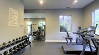 Located at 3590 Mary Adele Ave in Charleston, SC, this fitness center offers a well-appointed, single-floor exercise facility designed to support a comprehensive workout experience. The space is finished with durable, textured flooring suited for high-traffic athletic use, and the neutral gray walls create a clean, focused environment. Recessed lighting throughout ensures consistent illumination across the workout areas, while multiple windows allow natural light to filter in and provide views of the surrounding greenery, contributing to an open and energizing atmosphere. The facility is divided into distinct workout zones. The free weights area features a full dumbbell rack with a wide range of weight increments, ideal for strength training routines. The cardio section includes a stair climber and additional cardio equipment positioned near the windows. A dedicated strength training zone houses cable and pulley machines, a multi-function weight station, and additional resistance equipment, offering users a variety of exercise options. A large wall mirror in the strength area enhances the sense of space and allows for proper form monitoring during workouts. The layout provides ample room to move between stations comfortably. Overall, this fitness center is a practical, well-equipped space suited for residents seeking convenient on-site exercise amenities.