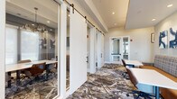 Located at 900 Elm Grove Ave in Gainesville, Georgia, this single-floor business center offers a thoughtfully designed workspace suited for collaboration and focused productivity. The entrance welcomes visitors with light hardwood flooring, soaring ceilings, and floor-to-ceiling glass doors that flood the space with natural light.

The centerpiece is a spacious conference room anchored by a solid wood communal table, surrounded by upholstered chairs and illuminated by a trio of striking black industrial pendant lights. Built-in shelving, a wall-mounted display screen, and a credenza with a shiplap accent wall complete the professional setting.

Private meeting rooms, enclosed by sleek sliding barn-style doors with glass panels, offer intimate spaces for smaller gatherings, each appointed with contemporary artwork and views of the surrounding greenery. Open co-working areas feature banquette-style seating with individual work tables, ideal for drop-in productivity sessions.

Throughout the space, a bold geometric-patterned carpet ties the aesthetic together, complemented by neutral walls, recessed lighting, and curated abstract artwork. A comfortable lounge area with plush blue accent chairs and side tables provides a relaxed setting for informal meetings. The overall ambiance is modern, polished, and highly functional.