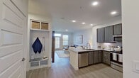 This single-story residence showcases a thoughtfully designed open-concept layout that seamlessly integrates the kitchen, dining, and living areas. The kitchen is a standout feature, equipped with dark wood-grain cabinetry extending to the ceiling, granite countertops, a subway tile backsplash, and a full suite of stainless steel appliances including a refrigerator, range, microwave, and dishwasher. A peninsula with an undermount sink provides additional workspace and casual seating potential while overlooking the living area, which benefits from natural light streaming through large windows with blinds.

Adjacent to the entry, a built-in mudroom nook offers practical storage with wall hooks, a bench, and overhead basket storage, adding functional organization to the entryway. Light wood-tone flooring runs consistently throughout the space, contributing to a cohesive and airy aesthetic.

The bedroom is a calm retreat featuring multiple windows dressed with sheer curtains, a ceiling fan, and ample wall space. The full bathroom includes an extended dual-sink vanity with granite countertops and dark cabinetry, a large mirror, and a tub-shower combination with tile surround. Recessed lighting throughout enhances the clean, contemporary ambiance of the space.
