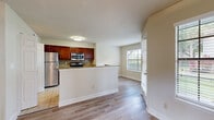 Located along N Military Trail in Boca Raton, Florida, this single-story residence offers a thoughtfully arranged layout with a variety of functional and aesthetic details throughout. The kitchen serves as a central hub of the home, featuring rich cherry-toned cabinetry, granite countertops, a mosaic tile backsplash, and a full suite of stainless steel appliances including a refrigerator, range, and built-in microwave. Tile flooring anchors the kitchen, which opens to an adjacent laundry area with in-unit washer and dryer access. A peninsula counter connects the kitchen to the main living area, which features light wood-tone flooring and a built-in bookshelf, adding both character and storage. Natural light filters through large windows fitted with blinds throughout the home. The living areas include a carpeted room with a sliding glass door that opens to a verdant outdoor setting with mature tropical landscaping. Bedroom spaces are well-sized, carpeted, and include multiple closets with built-in wire shelving and rod systems. The bathroom is finished with granite countertops, white cabinetry, tile flooring, a large vanity mirror, and a tub-shower combination with glass sliding doors.