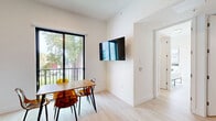 Located at 626 NW 11th Ave in Miami, FL, this modern single-floor unit offers 3 bedrooms and 3 bathrooms with a clean, contemporary aesthetic throughout. The open-plan living and kitchen area serves as the heart of the home, where light wood-grain cabinetry, dark stone countertops, and stainless steel appliances create a polished, functional kitchen. The living space accommodates comfortable seating and flows seamlessly toward a dedicated dining area, which features large black-framed sliding glass doors that open to an outdoor balcony, flooding the room with natural light and views of lush greenery. Light hardwood flooring runs consistently throughout the unit, reinforcing the bright, airy atmosphere. Each of the three bedrooms is efficiently designed with white walls, the same light flooring, individual wardrobes, and access to natural light via windows. One bedroom features a compact workspace with a shelving desk, ideal for remote work. The three bathrooms maintain the minimalist theme, each outfitted with white wall-mounted vanities, mirrored medicine cabinets, and clean tilework. The unit's entrance provides a practical transition point connecting all living spaces. Overall, the design emphasizes modern simplicity, natural light, and efficient use of space.