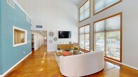 Located at 3587 Round Barn Blvd in Santa Rosa, California, this well-appointed single-floor space offers a thoughtfully designed layout across three distinct areas. The centerpiece is a dramatic lounge area defined by soaring vaulted ceilings and floor-to-ceiling wood-framed windows that flood the interior with abundant natural light and provide views of the surrounding greenery. Rich, polished concrete floors in a warm amber tone run throughout, lending a contemporary yet inviting character to the space. The lounge is styled with a curved sofa, glass coffee table, and an accent armchair, complemented by decorative starburst wall art and a wall-mounted flat-screen TV above a sleek wood credenza. Adjacent to the lounge, a kitchen features light wood cabinetry, stainless steel appliances including a full refrigerator, gas range, and microwave, as well as a marble-top island with bar seating — ideal for casual dining or entertaining. A vibrant teal accent wall adds a bold pop of color. The fitness center offers a dedicated workout area equipped with treadmills, an elliptical, and a stationary bike, all positioned alongside large windows and mirrored walls that enhance the sense of openness. Together, these spaces create a functional and stylish environment suited for community or professional use.