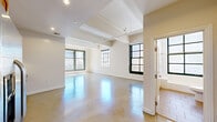 This single-floor loft-style unit blends industrial character with modern finishes to create a bright, versatile living space. The expansive main area is defined by polished concrete floors that reflect natural light throughout the day, while exposed structural beams overhead lend an industrial aesthetic to the otherwise clean, neutral interior. Large black-framed windows line the perimeter, offering sweeping urban views and flooding the space with abundant daylight. A Juliet balcony-style railing visible beyond the oversized windows adds a classic architectural touch.

The kitchen is well-appointed with rich warm-toned wood cabinetry, granite countertops, and a full suite of stainless steel appliances including a refrigerator with ice maker, electric range, built-in microwave, and dishwasher. A louvered door nearby provides convenient access to additional storage.

The bathroom is finished with large-format floor tiles, a soaking tub with a handheld shower fixture, a window that brings in natural light, and a vanity featuring granite countertops paired with warm wood cabinetry. The overall ambiance of the space is open, airy, and adaptable, making it well-suited for a variety of uses and layouts.