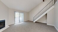 Located at 243 W 80th Ave in Denver, CO, this two-story unit offers a well-organized layout spread across a main floor and an upper loft level. The main floor hosts the living room, kitchen, bathroom, utility room, hallway, and multiple closets. The living room is a standout space, featuring soaring vaulted ceilings, plush wall-to-wall carpeting, and a corner fireplace with a tile surround. A large sliding glass door floods the room with natural light and provides views of the surrounding greenery. A sleek staircase with a black metal railing leads to the upper level. The kitchen is positioned conveniently off the main living area, while the bathroom features wood-look flooring, a dual-sink vanity with light-colored countertops, mirrored medicine cabinets, and louvered closet doors. Upstairs, the loft is an open, versatile space with vaulted ceilings, a ceiling fan, a built-in closet with bi-fold doors, and a window that brings in additional natural light. The metal railing along the loft overlook maintains a visual connection to the main floor below. Throughout the unit, neutral tones and clean finishes create a bright, cohesive atmosphere.