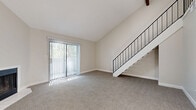 Located at 243 W 80th Ave in Denver, CO, this two-story unit offers a well-organized layout spread across a main floor and an upper loft level. The main floor hosts the living room, kitchen, bathroom, utility room, hallway, and multiple closets. The living room is a standout space, featuring soaring vaulted ceilings, plush wall-to-wall carpeting, and a corner fireplace with a tile surround. A large sliding glass door floods the room with natural light and provides views of the surrounding greenery. A sleek staircase with a black metal railing leads to the upper level. The kitchen is positioned conveniently off the main living area, while the bathroom features wood-look flooring, a dual-sink vanity with light-colored countertops, mirrored medicine cabinets, and louvered closet doors. Upstairs, the loft is an open, versatile space with vaulted ceilings, a ceiling fan, a built-in closet with bi-fold doors, and a window that brings in additional natural light. The metal railing along the loft overlook maintains a visual connection to the main floor below. Throughout the unit, neutral tones and clean finishes create a bright, cohesive atmosphere.