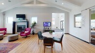 Located at 1443 Devon Ln in Harrisonburg, Virginia, this single-floor community clubhouse is a thoughtfully designed gathering and amenity space that blends bold aesthetics with practical functionality. The interior showcases a dynamic mix of design styles unified by vibrant color palettes, vaulted ceilings with exposed beams, and abundant natural light streaming through large windows overlooking outdoor pool and landscape views.

The main lounge area features a teal sectional sofa, colorful accent chairs, a patterned area rug, and a striking dark accent wall adorned with curated artwork and a neon sign, creating a lively social atmosphere. A separate collaborative lounge offers high-back privacy seating pods, chartreuse accent chairs, and modular furniture arranged for both individual focus and group interaction, all set against graphic patterned carpeting.

A cozy seating nook, illuminated by sculptural pendant lights, provides intimate views of the pool area. The space also includes a modern kitchenette with navy cabinetry, quartz countertops, and a large communal dining table beneath industrial pendant lighting — ideal for casual gatherings. A fireplace lounge with vaulted ceilings and mid-century furnishings adds warmth and character. Connecting corridors with sleek linear lighting and built-in workstation areas complete this well-appointed community facility.