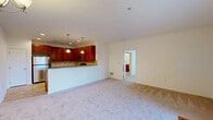This single-floor residence offers a thoughtfully designed open-concept layout that seamlessly connects the kitchen and living areas. The kitchen is outfitted with rich cherry-toned cabinetry, granite countertops, a tile backsplash, and a full suite of stainless steel appliances, including a gas range, microwave, and refrigerator. A peninsula with pendant lighting serves as both a functional workspace and casual dining area. The kitchen flows directly into the carpeted living space, which is anchored by a chandelier and French doors that open to an outdoor balcony, filling the room with natural light.

The bedroom is generously sized, featuring multiple windows on two walls that provide ample natural light and views of greenery. It connects to a large walk-in closet with built-in wire shelving and a private en-suite bathroom. The bathroom includes a dual-sink vanity with cherry cabinetry, a large mirror, and a tiled walk-in shower with sliding glass doors and tile flooring.

A dedicated laundry room houses a full-size washer and dryer alongside wire shelving for additional storage. Throughout, neutral tones, plush carpet, and tile flooring create a clean and cohesive aesthetic.