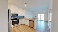 This well-appointed 1-bedroom, 1-bathroom residence in Stevensville, MD offers a thoughtfully designed open-concept layout that maximizes functionality and flow. The kitchen is a standout feature, outfitted with white shaker cabinetry, a tiled backsplash, stone countertops, and a full suite of stainless steel appliances including a refrigerator, electric range, microwave, and dishwasher. Light wood-tone flooring runs throughout the main living areas, lending warmth and visual continuity. The kitchen opens seamlessly into the living area, which benefits from natural light and direct access to a private balcony through sliding glass doors. The bedroom is a comfortable, carpeted retreat featuring large windows that frame outdoor views of the surrounding landscape, allowing abundant natural light to fill the room. A dedicated closet provides practical storage. The bathroom is finished with tile flooring, a soaking tub, a separate tiled shower with a grab bar, and clean white walls that contribute to a crisp, modern aesthetic. The overall design is clean and contemporary, with a neutral color palette throughout that creates a bright and welcoming atmosphere.