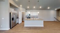 Located at 5800 41st St S in Fargo, North Dakota, this single-floor home showcases a thoughtfully designed open-concept layout with contemporary finishes throughout. The living area is a standout feature, boasting vaulted ceilings with recessed lighting, wood-look flooring, a built-in fireplace flanked by open shelving, and a sliding glass door that invites natural light and outdoor access.

The kitchen is well-appointed with white cabinetry, stainless steel appliances including a refrigerator and range, a large central island with an integrated sink and pendant lighting overhead, and a dedicated walk-in pantry for generous storage. The kitchen flows seamlessly into the dining and living areas, creating a cohesive entertaining space.

Multiple bedrooms feature neutral-toned carpet, white blinds, and multiple windows that fill each room with natural light. At least one bedroom includes a walk-in closet. The bathrooms are finished with white shaker-style cabinetry, gray countertops, and modern fixtures, with one bathroom featuring an illuminated vanity mirror. Wood-look flooring runs throughout the bathrooms, complementing the home's consistent, clean aesthetic.