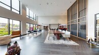 Located at 500 Parq Ln in Parsippany, NJ, this expansive amenity lounge is a thoughtfully designed communal space that combines modern aesthetics with versatile functionality. Soaring double-height ceilings amplify the sense of openness throughout, while large floor-to-ceiling windows and sliding glass doors flood the interior with natural light and offer direct views of an outdoor patio and landscaped courtyard.

The main lounge area is anchored by a substantial wood conference-style table surrounded by upholstered chairs, making it ideal for collaborative work or group gatherings. Sleek dark tile flooring runs throughout, complemented by layered area rugs that define distinct seating zones. A vertical wood slat accent wall adds warmth and architectural interest.

A sophisticated lounge nook features plush gray sofas, a striking sputnik chandelier, and a large wall-mounted TV set against a marble and wood feature wall. Adjacent to this is a dedicated billiards area and a bar-height lounge zone near the outdoor access points.

A standout feature is the private golf simulator room, complete with a projected screen, synthetic turf, and bar stool seating — perfect for recreation. A separate café area with pendant lighting and bar seating is accessible through glass-paneled sliding doors, rounding out this well-appointed amenity space.