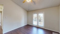 This two-bedroom, one-bathroom home in Lewisville, TX offers a well-organized single-floor layout with a thoughtful mix of finishes and functional spaces. The open living area is a highlight, featuring vaulted ceilings, a ceiling fan, a textured ceiling, and rich dark hardwood-style flooring. A classic brick wood-burning fireplace serves as a focal point, while French doors flood the space with natural light and provide direct access to a private balcony with outdoor views. The layout flows seamlessly into a combined dining and kitchen area. The galley-style kitchen is lined with warm wood cabinetry, ample counter space, and white appliances including a refrigerator, range, microwave, and dishwasher, complemented by a pass-through window connecting to the living area. Both bedrooms are carpeted and well-sized, each with access to closet space. The primary bedroom includes a spacious walk-in closet with wire shelving. A second bedroom features a ceiling fan and natural light from a window. The full bathroom includes a shower-tub combination. Additional highlights include three closets for storage, a dedicated laundry area, and a hallway connecting the private quarters. The neutral color palette throughout creates a clean, versatile living environment.