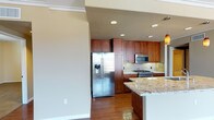 This single-story space showcases a thoughtfully designed kitchen as its centerpiece. Rich, warm-toned wood cabinetry lines the walls, extending floor to ceiling to maximize storage capacity. The cabinetry is complemented by granite countertops featuring intricate veining in cream and earthy tones, adding a touch of elegance to the space. A kitchen island with matching granite provides additional workspace and casual seating potential.

The kitchen is equipped with a full suite of stainless steel appliances, including a side-by-side refrigerator with water and ice dispenser, a built-in microwave, and a gas range. A classic tile backsplash in a neutral tone ties the design elements together seamlessly. Recessed lighting installed throughout the ceiling ensures even, practical illumination across the entire workspace.

The flooring features rich hardwood in a warm brown tone, creating a cohesive and inviting aesthetic that complements the cabinetry. Smooth, neutral-painted walls provide a clean contrast to the warm wood tones. The textured ceiling adds subtle visual interest overhead, while a pendant light fixture is partially visible, hinting at additional decorative lighting accents within the space.