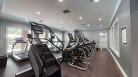 Located at 100 Hawthorne Way in Lawrence, Massachusetts, this fitness center offers a well-appointed, single-floor space designed to support a wide range of workout routines. The facility is finished with durable rubber flooring throughout and painted in cool gray tones, creating a focused and energizing atmosphere. Recessed lighting illuminates the space evenly, complemented by natural light streaming in through multiple windows that provide views of surrounding greenery.

The cardio zone features a generous lineup of Matrix treadmills, elliptical trainers, stair climbers, and stationary bikes, all arranged to maximize space and accessibility. A dedicated free weights area includes a full rack of dumbbells spanning a wide weight range, an adjustable workout bench, and kettlebells, catering to strength training needs. The strength zone is further equipped with a cable machine and additional weight training apparatus, supported by floor-to-ceiling mirrors that enhance the sense of space and allow for form monitoring.

Motivational wall decals add character to the environment, with phrases promoting health, strength, happiness, confidence, and results. A medicine ball storage rack with colorful stability balls rounds out the functional training offerings. The layout flows intuitively between zones, making the fitness center an efficient and inspiring place to train.