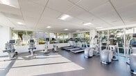 Located at 2420 Cardinal Drive in San Diego, California, this single-story fitness center offers a well-appointed space designed to support a comprehensive workout experience. The facility is divided into two distinct areas: a main gym floor and a separate studio room.

The main gym is spacious and bright, featuring a drop-panel ceiling with recessed fluorescent lighting that evenly illuminates the floor. Large windows line multiple walls, flooding the space with abundant natural light and providing views of lush, green outdoor landscaping. The durable rubber flooring supports a wide array of cardio and strength equipment, including multiple treadmills, elliptical machines, stationary and recumbent bikes, a cable machine, weight benches, and a full dumbbell rack. Floor-to-ceiling mirrors along one wall enhance the sense of openness and allow users to monitor their form.

The secondary room features warm hardwood-style flooring, a drop-panel ceiling with built-in speakers, and a distinctive accent wall adorned with geometric hexagonal acoustic or decorative panels. This room is ideal for yoga, stretching, or group fitness classes. A glass door provides direct access to the outdoor area, further connecting the interior to the surrounding environment. Together, the two areas create a versatile, light-filled fitness facility well-suited for a variety of exercise routines.