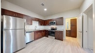 This thoughtfully designed 1-bedroom, 1-bathroom unit offers a functional and modern living experience across a single floor. The open-concept layout seamlessly connects the kitchen and living room, creating a bright and airy atmosphere enhanced by recessed lighting and light wood-style flooring that runs throughout the entire unit.

The kitchen is a standout feature, showcasing rich dark wood cabinetry with brushed nickel hardware, light granite countertops, a tile backsplash, and a full suite of stainless steel appliances including a refrigerator, dishwasher, microwave, and electric range. Ample cabinet storage and counter space make this kitchen as practical as it is attractive.

The open living room is filled with natural light from large windows and a glass door, and is fitted with a ceiling fan for added comfort. The bedroom is a comfortable, well-proportioned room with a window offering outdoor views and the same light flooring that unifies the space.

The bathroom maintains the design consistency of the unit with a dark wood vanity, granite countertop, a large mirror, and a full shower-tub combination with white tile surround. Clean lines and neutral tones throughout give this unit a fresh, move-in-ready appeal.