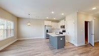 Located at 4040 Candleberry Gdn in North Augusta, South Carolina, this two-story home offers a clean, modern design with thoughtful finishes throughout. The open-concept main living area is anchored by a well-equipped kitchen featuring white shaker cabinetry, a subway tile backsplash, quartz countertops, stainless steel appliances including a French door refrigerator and electric range, and a central island with a built-in sink. Elegant pendant lighting and recessed fixtures illuminate the space, which flows seamlessly into the dining and living areas. Multiple windows and a rear door flood the main level with natural light and provide direct access to a fenced backyard with a well-maintained lawn. Light wood-look flooring runs throughout the main living spaces, complementing the neutral gray-beige wall tones. Bedrooms feature plush carpeting, ceiling fans, natural light from large windows, and walk-in closets. The primary bathroom is outfitted with a dual-sink vanity, white cabinetry, and a large mirror, while a secondary bathroom offers a full tub-shower combination. The attached garage includes an automatic opener, an electrical panel, and a water heater, providing practical utility space. Crown molding, panel-style interior doors, and consistent finishes contribute to a cohesive, move-in-ready aesthetic throughout the home.