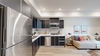 Located in the heart of Los Angeles, this well-designed one-bedroom, one-bathroom residence offers a thoughtful layout across a single floor. The open-concept kitchen and living area serves as the centerpiece of the home, featuring dark, modern cabinetry with silver trim, white countertops, a tile backsplash, and a full suite of stainless steel appliances including a refrigerator, dishwasher, gas range, and built-in microwave. Light wood-style flooring runs throughout, lending warmth and continuity to the space. The living area benefits from floor-to-ceiling sliding glass doors that open to a private balcony, filling the room with natural light and offering open views of the surrounding Los Angeles cityscape. The bedroom is a calm, well-proportioned retreat with clean white walls, recessed lighting, and a mirrored sliding closet. A second closet and an in-unit laundry area add practical convenience. The bathroom features a wall-mounted sink, large mirror, and a clean, minimalist aesthetic with light wood flooring. A hallway connects the rooms efficiently, with a distinctive dark wood accent panel adding a modern design touch. The space is polished, functional, and well-suited to modern urban living.
