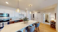 This thoughtfully designed single-floor residence offers a cohesive blend of modern finishes and comfortable living spaces. The open-concept kitchen is a standout feature, showcasing a striking two-tone design with crisp white upper cabinetry and warm wood lower cabinets, quartz countertops, and a generously sized island with seating for multiple guests. Pendant lighting with glass fixtures adds an elegant touch, while stainless steel appliances and a tile backsplash complete the functional yet stylish space. Light hardwood flooring flows seamlessly into the adjacent living area, which is bright and welcoming, featuring a front-facing window that brings in natural light. The living room offers ample space for comfortable seating arrangements and is accented with soft, neutral tones. Two well-proportioned bedrooms each feature windows with outdoor views, allowing natural light to fill the rooms. The primary bathroom includes a walk-in shower with a sleek black-framed glass enclosure and a white vanity, while the second bathroom offers a full tub-shower combination with clean, neutral finishes. Dark wood-look flooring in the bathrooms provides a tasteful contrast to the light, airy palette found throughout the rest of the home.