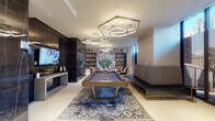 Located at 1909 Walnut Street in the heart of Philadelphia's Rittenhouse Square neighborhood, this sophisticated amenity lounge delivers a premium communal experience defined by high-end finishes and thoughtful design. The space is anchored by a central billiards area, where a full-size pool table rests atop an ornate blue medallion rug beneath a striking arrangement of geometric hexagonal gold-and-white pendant light fixtures that illuminate the room with a warm, modern glow. Floor-to-ceiling windows along one side of the space flood the interior with natural light while offering expansive views of the Philadelphia skyline, creating an ideal setting for intimate conversation areas furnished with cream upholstered chairs and a sleek marble-topped table. The lounge area features deep, plush sectional seating in cream and teal, arranged around a linear fireplace framed in dramatic dark veined marble that extends across the wall, with a wall-mounted flat-screen TV above. Built-in bookshelves with a nature-inspired mural serve as a focal point in the game area, adding an artistic layer to the space. The catering kitchen is outfitted with dark stone countertops, warm wood cabinetry, and floor-to-ceiling glazing that continues the panoramic city views. Large-format porcelain tile flooring and reflective dark marble wall panels unify the space with a polished, contemporary aesthetic throughout.